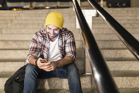 UK, London, Mann sitzt auf einer Treppe und schaut auf sein Handy während einer nächtlichen Fahrt, lizenzfreies Stockfoto