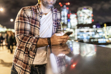 UK, London, close-up of man leaning on a railing with cell phone with city lights in background - WPEF01216