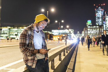 UK, London, lächelnd Mann mit Telefon auf der Straße in der Stadt in der Nacht - WPEF01220