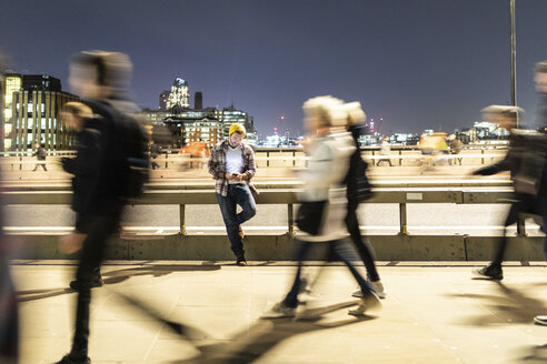 UK, London, man looking at his phone with blurred people walking on the pavement - WPEF01222
