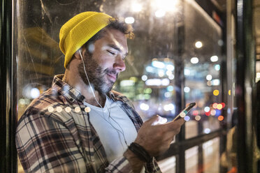 UK, London, smiling man at the bus stop looking at his phone - WPEF01223