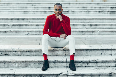 Porträt eines stilvollen jungen Mannes mit rotem Pullover und Socken auf einer Treppe sitzend - JSMF00709