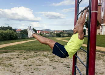 Muskulöser Mann trainiert an einem Klettergerüst im Freien - MGOF03847