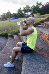 Muscular man having a break from exercising drinking water - MGOF03850