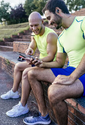 Two smiling athletes sharing smartphones after workout - MGOF03852