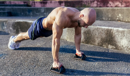 Barechested muscular man doing push-ups outdoors - MGOF03864