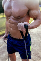 Mittelteil eines barbusigen, muskulösen Mannes, der mit einem Expander im Freien trainiert - MGOF03876