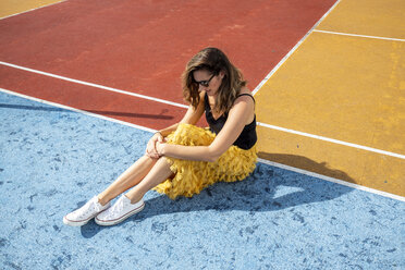 Frau mit Sonnenbrille sitzt auf einem Sportplatz - DAWF00792