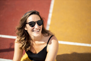 Portrait of happy woman wearing sunglasses on a sports field - DAWF00793