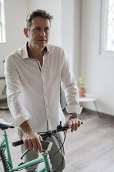 Portrait of businessman with bicycle in office - GIOF05060