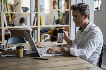 Businessman holding coffee mug using laptop at desk - GIOF05063