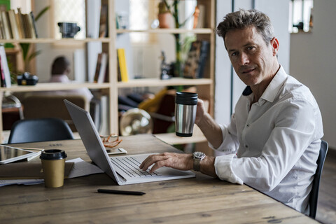 Porträt eines Geschäftsmannes mit Laptop am Schreibtisch, lizenzfreies Stockfoto