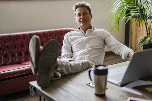 Porträt eines Geschäftsmannes, der mit den Füßen auf dem Schreibtisch sitzt - GIOF05066