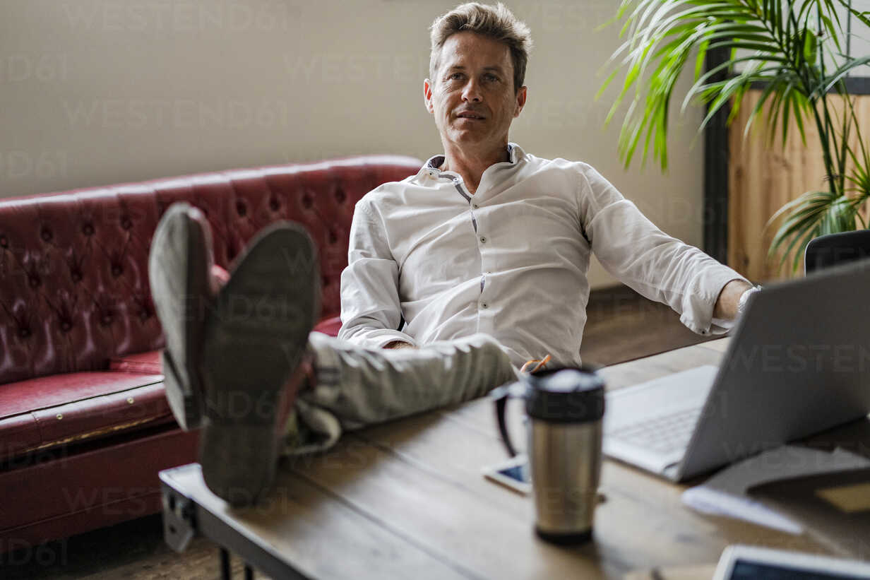 Businessman sitting in office with feet up on desk - Stock Photo