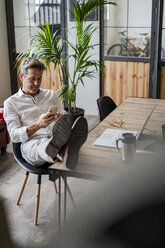 Geschäftsmann sitzt mit den Füßen auf dem Schreibtisch und benutzt ein Mobiltelefon - GIOF05070