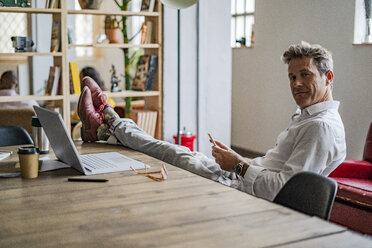 Porträt eines Geschäftsmannes, der mit den Füßen auf dem Schreibtisch sitzt - GIOF05071