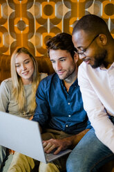 Three people sitting on couch in vintage living room sharing laptop - GIOF05083