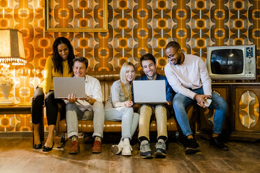 Gruppe von lächelnden Menschen sitzen auf der Couch in Vintage-Wohnzimmer teilen Laptops - GIOF05084