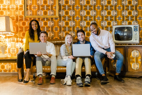 Gruppe von lächelnden Menschen sitzen auf der Couch im Vintage-Wohnzimmer mit Laptops - GIOF05085