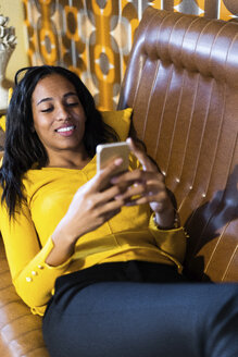 Lächelnde Frau liegt auf der Couch im Vintage-Wohnzimmer und benutzt ein Mobiltelefon - GIOF05087