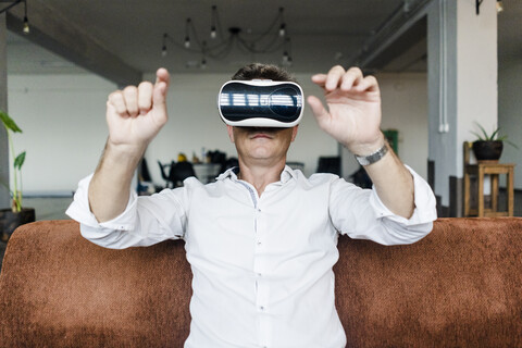 Mature man wearing VR glasses sitting on couch in a loft stock photo