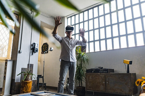 Mature man wearing VR glasses standing at the window in a loft - GIOF05099