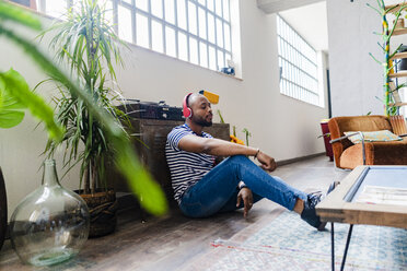 Young man with headphones sitting on floor in a loft - GIOF05109