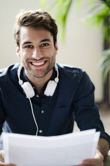 Porträt eines lächelnden jungen Mannes mit Kopfhörern und Papieren - GIOF05135