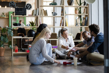 Business team sitting on floor discussing documents in loft office - GIOF05137