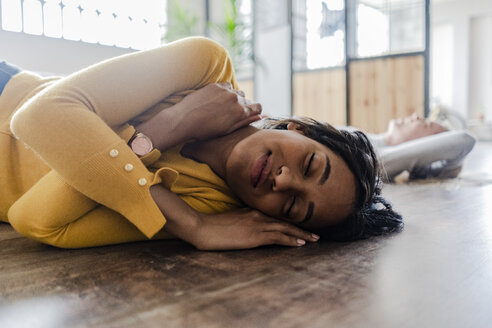 Lächelnde junge Frau auf Holzboden liegend mit geschlossenen Augen - GIOF05141