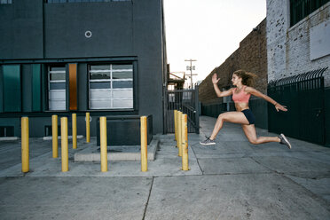 Female athlete running on sidewalk past industrial buildings. - MINF09816