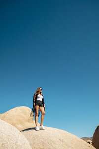 USA, California, Los Angeles, woman standing on rock under blue sky in Joshua Tree National Park - DAWF00859