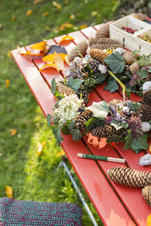 Herbstlicher Kranz mit Hortensien, Tannenzapfen und Efeu auf dem Gartentisch - OJF00290