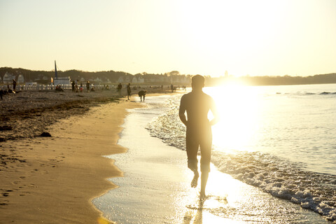 Mann joggt am Strand bei Sonnenuntergang, lizenzfreies Stockfoto