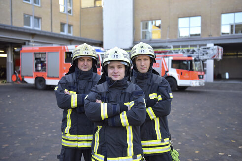 Porträt von drei selbstbewussten Feuerwehrleuten, die vor einem Feuerwehrauto auf dem Hof stehen - LYF00844