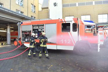 Zwei Feuerwehrleute stehen auf dem Hof und üben mit Löschwasser - LYF00846