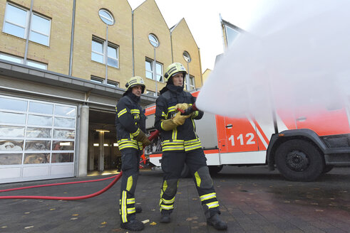 Zwei Feuerwehrleute stehen auf dem Hof und üben mit Löschwasser - LYF00847