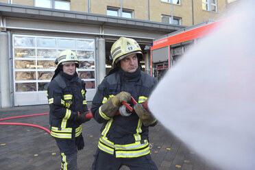 Two firefighters standing on yard exercising with extinguishing water - LYF00848