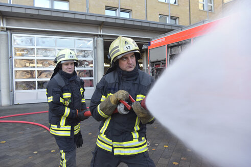 Zwei Feuerwehrleute stehen auf dem Hof und üben mit Löschwasser - LYF00848