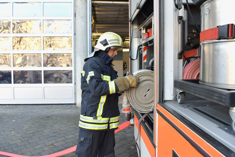 Feuerwehrmann nimmt Feuerlöschschlauch vom Feuerwehrauto, lizenzfreies Stockfoto