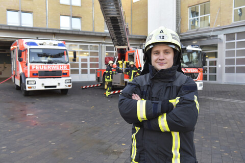 Portrait of confident firefighter in front of fire engine with colleagues in background stock photo