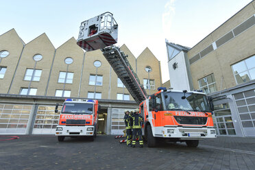 Zwei Feuerwehrleute stehen auf dem Hof an einem Löschfahrzeug und bereiten sich auf einen Einsatz vor - LYF00856