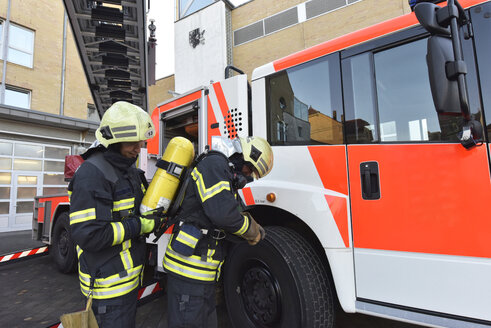 Zwei Feuerwehrleute an einem Löschfahrzeug bei der Vorbereitung eines Einsatzes - LYF00857