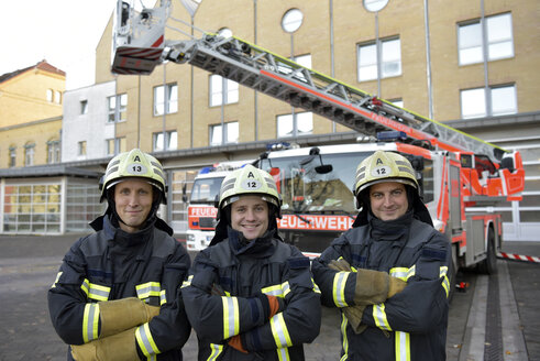 Porträt von drei lächelnden Feuerwehrleuten, die auf dem Hof vor einem Feuerwehrauto stehen - LYF00859