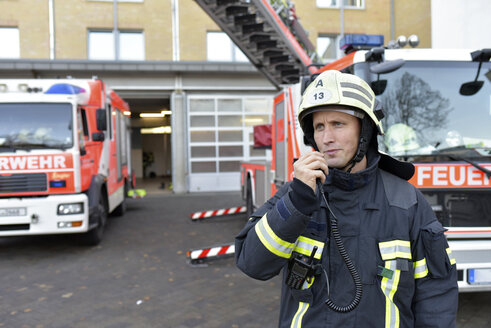 Firefighter standing on yard at fire engine using walkie talkie - LYF00860