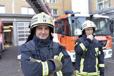 Portrait of two confident firefighters in front of fire engine - LYF00861