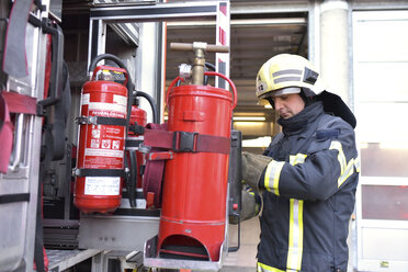 Firefighter standing at fire engine with fire extinguisher - LYF00863
