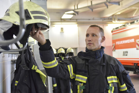 Feuerwehrmann nimmt Helm vom Regal in der Feuerwache, lizenzfreies Stockfoto