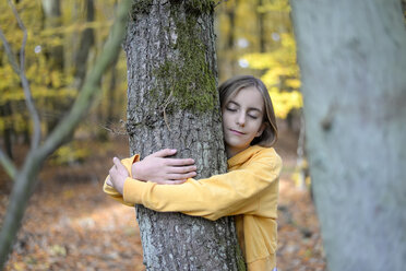 Portrait of girl with eyes closed hugging tree in autumnal forest - BFRF01942