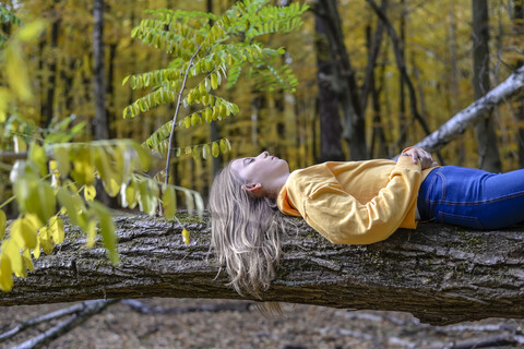 Mädchen liegt auf einem Baumstamm im herbstlichen Wald und entspannt sich, lizenzfreies Stockfoto